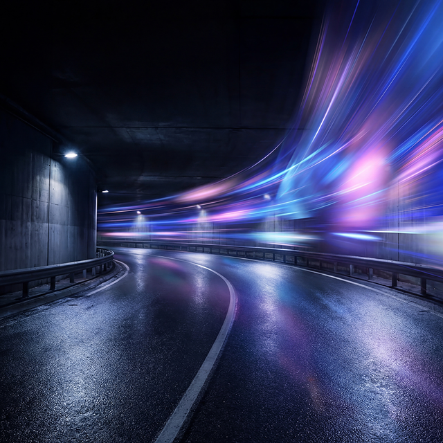 Inside a futuristic curving tunnel with guardrails on both sides and blue and purple light streaks