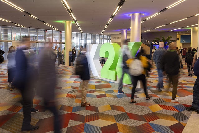 Blurred people walking past a lifesize floor sign that says K26