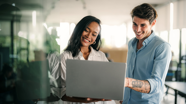 Two co-workers smiling at a laptop in an office setting 