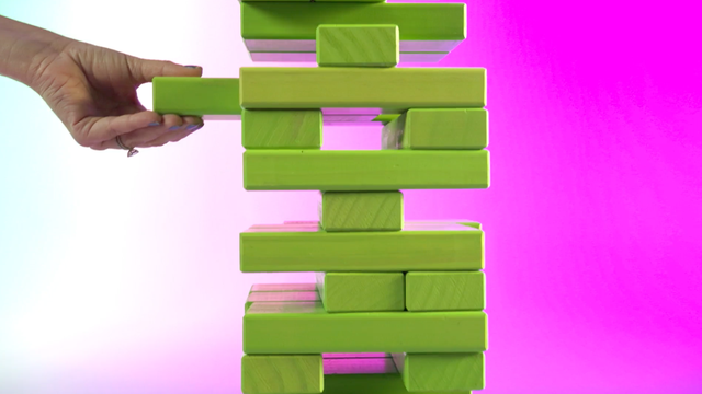 A hand removing a plank from a Jenga tower